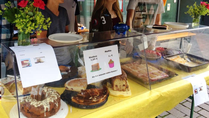 Stand auf dem Wochenmarkt mit gelber Tischdecke, durchsichtigem Spuckschutz undund verschschiedenen Kuchen ind er Auslage