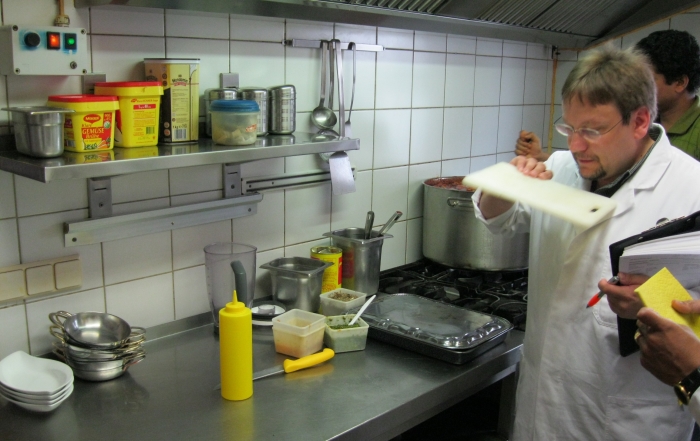 Lebensmittelkontrolleur bei der Arbeit prüft in einer weißgekachelten Restaurantküche ein Küchenbrett aus Kunststoff