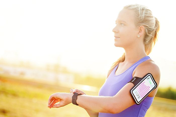 Blonde Freizeitsportlerin in Sportkleidung ist auf Wiese unterwegs mit Smartwatch und Fitness-Armband