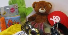 Diverses Kinderspielzeug auf einem Haufen, u. a. ein Teddybär, eine Kindersonnenbrille, ein Käppi, ein Kinderbilderbuch, eine Sandale