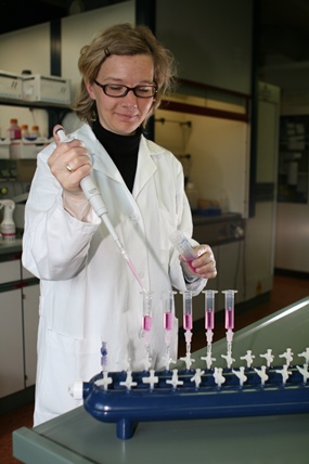 Laborantin mit Brille und weißem Laborkittel füllt Substanzen in Probegläser