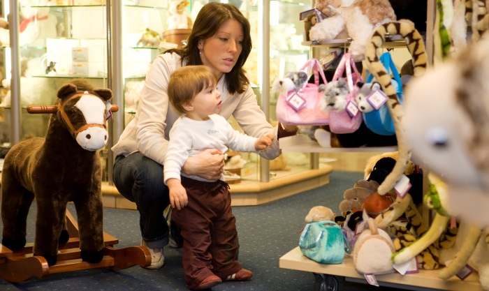 Kleinkind mit Mama im Spielzeugladen mit Stofftieren, wie einem braunen Rollpony