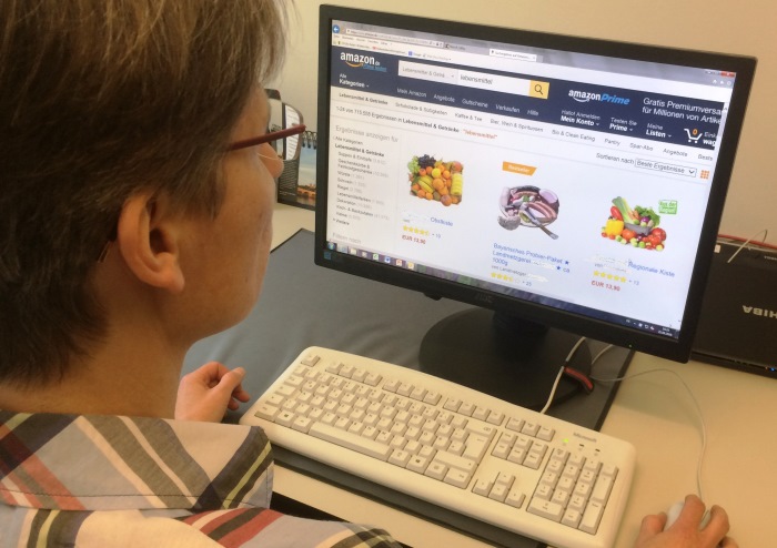 Eine Frau mit Brille sitzt vor einem Bildschirm mit Tastatur und studiert online-Angebote zum Einkauf