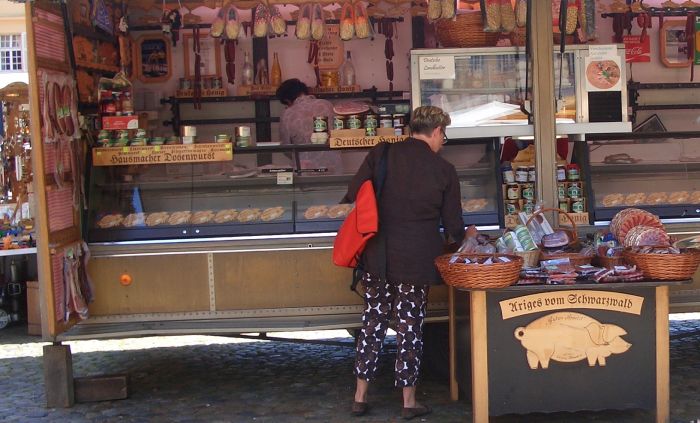 Metzgerstand auf einem Wochenmarkt mit älterer Kundin beim Begutachten der WAre