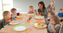 Mehrere Kleinkinder zu Tisch beim Essen in der Kindertagesstätte mit 2 Erzieherinnen