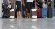 Unterleibe und Beine von wartenden Fluggästen in einer Schlange mit diversen Rollkoffern